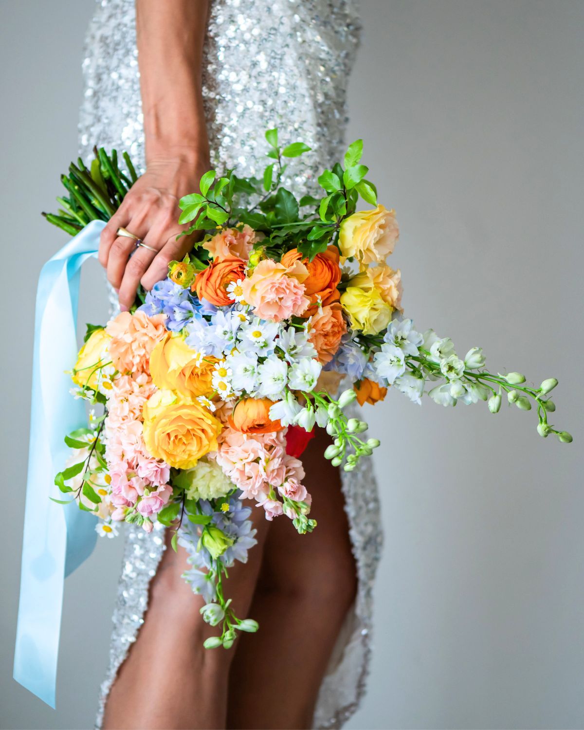 bride holding colourful wedding bouquet with orange ranunculus yellow roses and blue delphinium